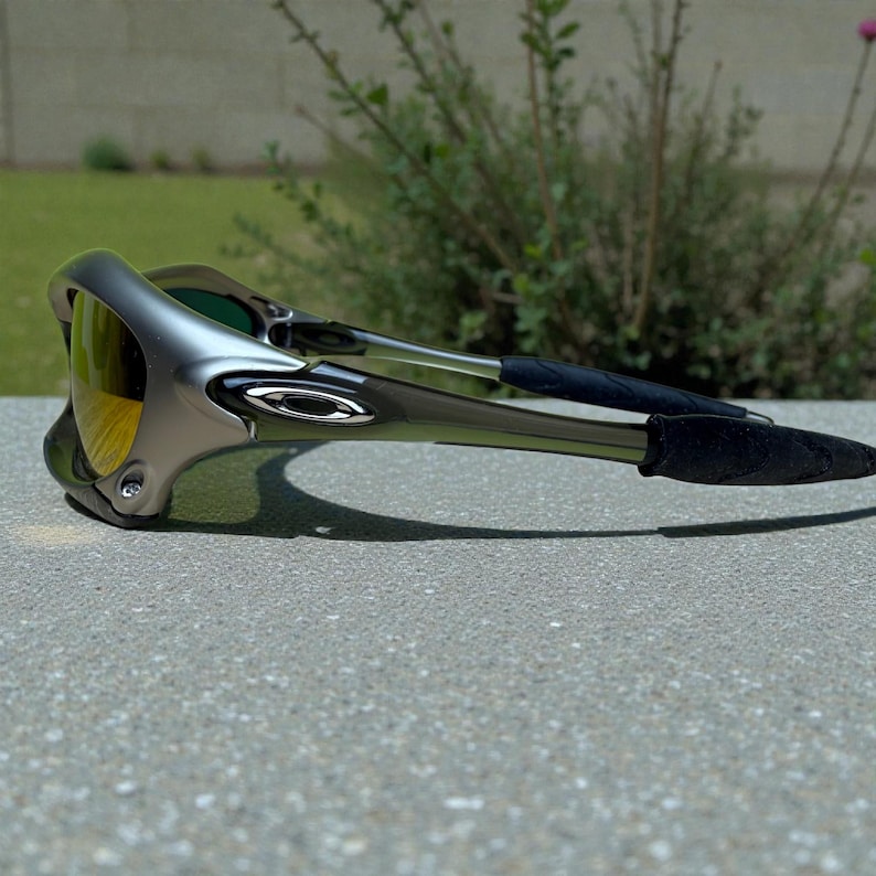 May include: Gray and black Oakley sunglasses with yellow-tinted lenses. The sunglasses have a curved, aerodynamic design with the Oakley logo on the temples. The arms have black rubber grips for a secure fit.