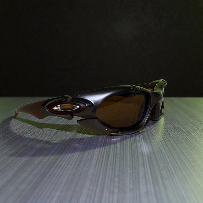 May include: A pair of black and brown sunglasses with a sporty design. The sunglasses have brown lenses and a dark frame with a red and gold logo on the side. The arms are a reddish-brown color.