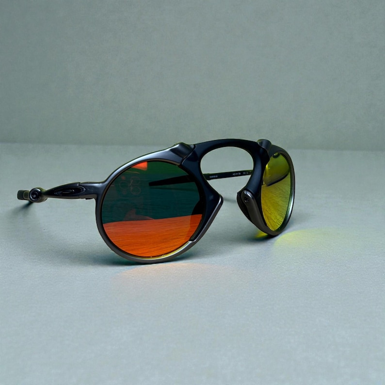 May include: Black sunglasses with a unique frame design and orange and yellow lenses. The lenses have a reflective coating. The sunglasses are set against a neutral background.