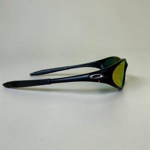 May include: Black sunglasses with a curved frame and yellow-green lenses. The sunglasses have a sleek, modern design with a silver accent on the frame. The arms are thin and extend back to the ear pieces.