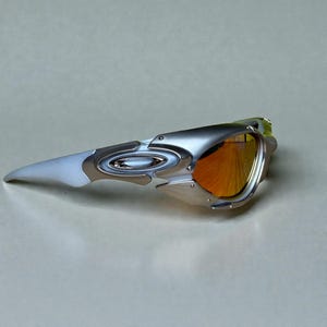 May include: Silver and white sunglasses with orange-tinted lenses. The sunglasses have a sleek, modern design with a metallic frame and a distinctive shape. The lenses are a vibrant orange color, offering a bold contrast to the frame.