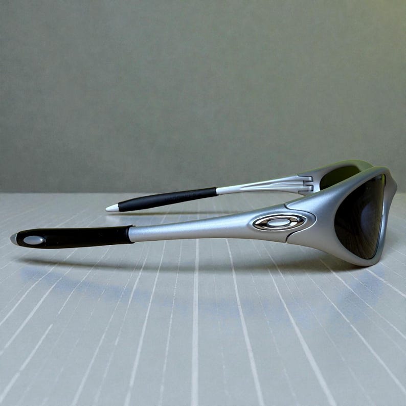 K&ouml;nnte beinhalten: Silberfarbene Sonnenbrille mit schwarzen Gl&auml;sern und schwarzen B&uuml;geln. Die Sonnenbrille hat ein schlankes, modernes Design mit einem silbernen Rahmen und einem kleinen Logo. Die dunklen Gl&auml;ser bieten Schutz vor der Sonne.