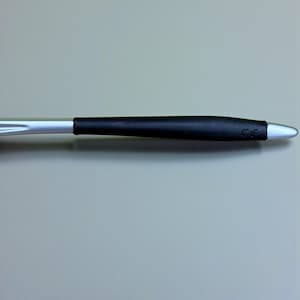 Op de afbeelding: Een zilveren en zwarte pen met een zwarte rubberen grip. De pen heeft een zilveren punt en de letters "CE" zijn gedrukt op de zwarte grip. De pen staat tegen een grijze achtergrond.