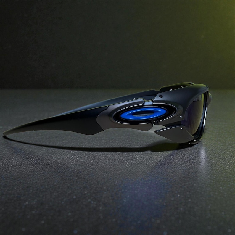 May include: Black and gray sunglasses with a futuristic design. The sunglasses feature a blue circular accent and dark lenses. The sleek, aerodynamic shape suggests a sporty or high-performance aesthetic.