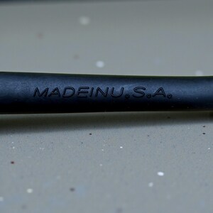 Op de afbeelding: Close-up van een zwart object met de in reli&euml;f aangebrachte tekst "MADE IN U.S.A.". Het object lijkt een handvat of onderdeel van een gereedschap te zijn, met een matte afwerking. De achtergrond is een lichtgrijze ondergrond.
