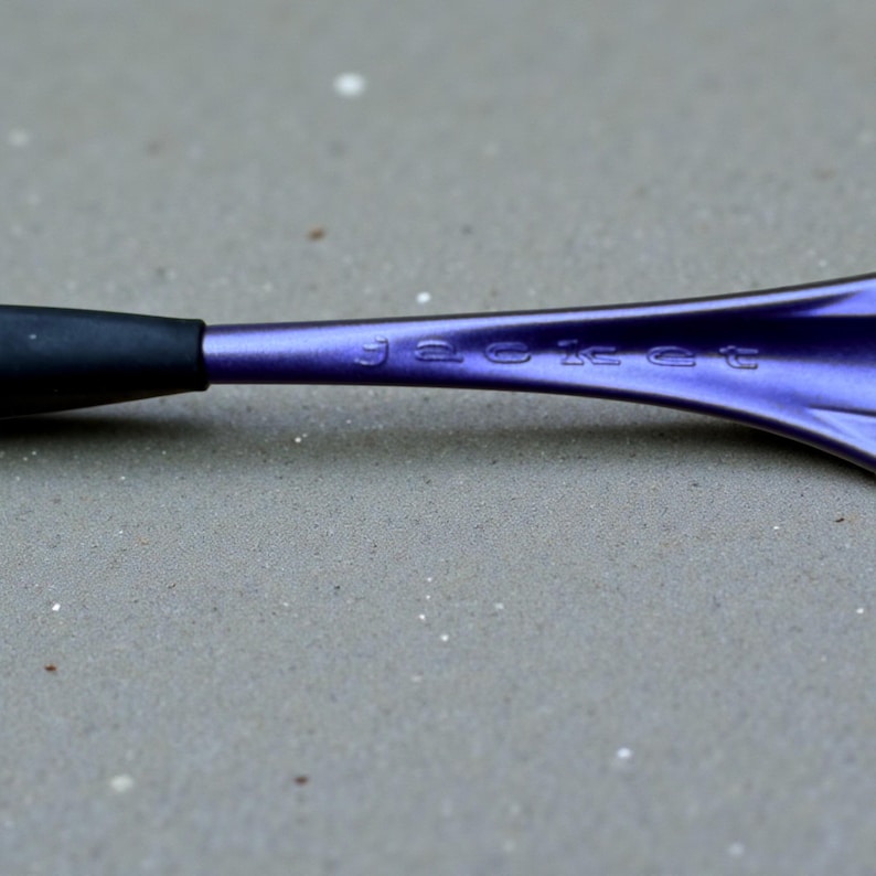 May include: Close-up of a purple metal object with the word "jacket" engraved on it. The object has a black handle and a flared, curved design. The surface appears to have a metallic sheen.