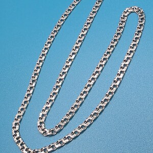 May include: A silver-colored chain necklace with a textured, interlocking link design. The necklace is displayed against a solid blue background, showcasing its intricate pattern and metallic sheen. The clasp is visible at the top.