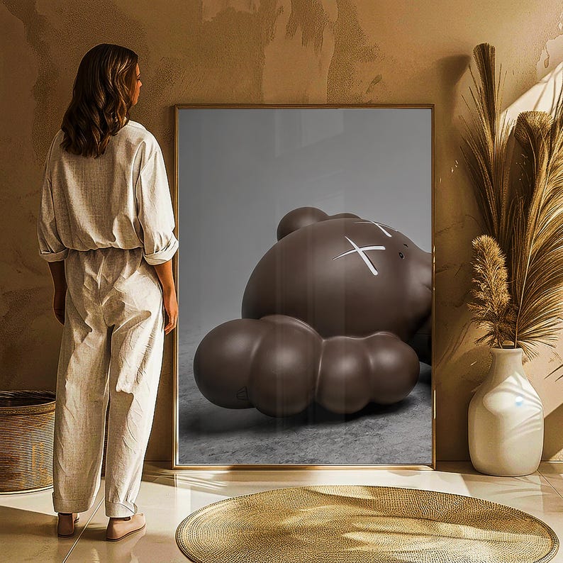 May include: A framed artwork featuring a large, brown, cartoon-like bear figure with white 'X' marks for eyes. The bear is lying down. The artwork is in a room with a woman standing nearby.