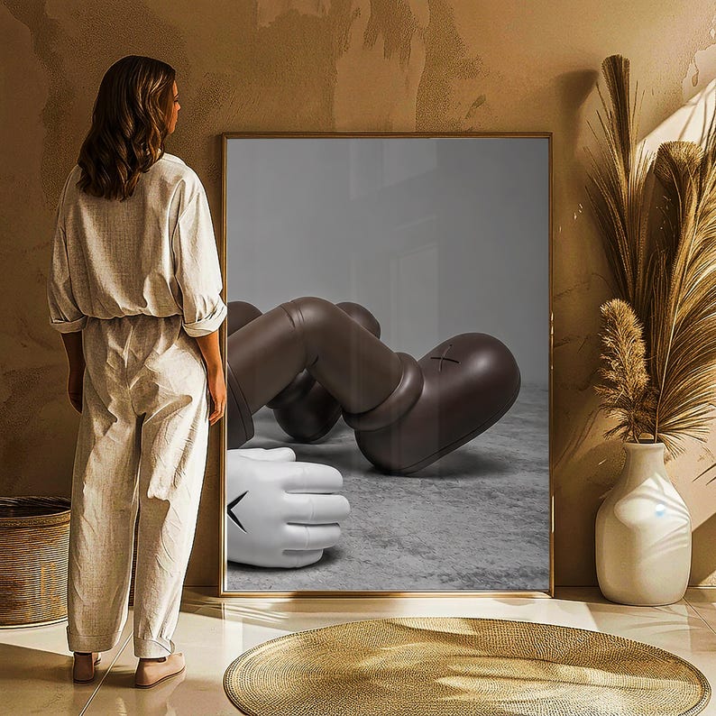 May include: A framed artwork featuring a brown and white cartoon figure in a relaxed pose. The figure has large, rounded features and a stylized appearance. The artwork is displayed in a room with neutral tones and decorative elements.