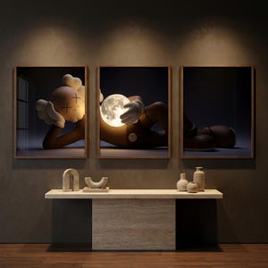 May include: A triptych of framed wall art featuring a brown cartoon character with X-shaped eyes lying down and holding a glowing, cratered moon. The artwork is displayed above a light beige stone console table with small decorative ceramic vases.