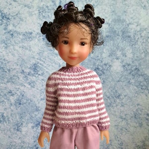 May include: A doll with brown curly hair wearing a pink and white striped sweater and pink shorts.