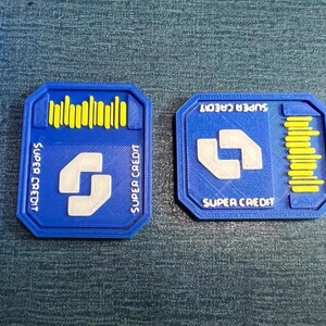 May include: Two blue rectangular tokens with the words "SUPER CREDIT" and a white stylized "S" shape. One token has yellow vertical lines, the other has yellow horizontal lines. The tokens are on a blue surface.
