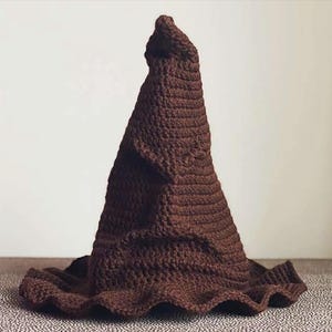 May include: A brown, handmade crochet hat with a pointed top and a wide, ruffled brim. The hat is made of a textured yarn, and the color is a rich, dark brown. The hat is likely for costume or cosplay.