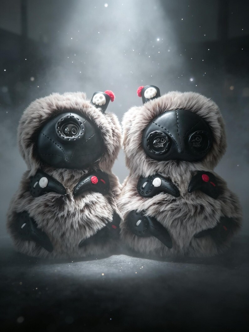 May include: Two plush creatures covered in long, light brown faux fur. Each has a black leather-like face with button eyes, stitched details, and small black appendages. One features a single central eye, while the other has two button eyes.