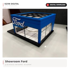 May include: A 3D printed model of a Ford dealership showroom featuring a blue exterior with the white Ford logo on the front facade, large glass-style windows, and a black roof grid structure, all mounted on a solid black rectangular base.