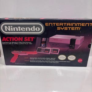 May include: A Nintendo Entertainment System Action Set box featuring a grey and black game console, two rectangular controllers, a red and grey Zapper light gun, and a Duck Hunt and Super Mario Bros. game cartridge. The box has black and purple graphics.