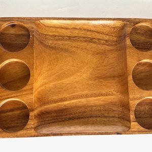 May include: A rectangular wooden serving tray with a central recessed area and six circular indentations. The tray is made of light brown wood with visible grain patterns.