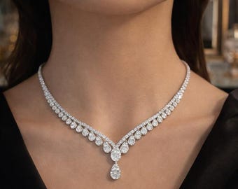 May include: A dazzling diamond necklace featuring a delicate design. The necklace has a V-shaped arrangement of round and pear-shaped diamonds, with a single pear-shaped diamond pendant. The diamonds sparkle against a dark background.