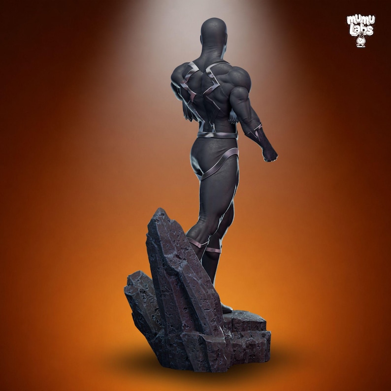 Puede incluir: Estatua de figura negra con detalles plateados, posada sobre una base rocosa contra un fondo degradado naranja. La figura tiene una complexi&oacute;n musculosa y lleva un traje ajustado. Es un art&iacute;culo de colecci&oacute;n.