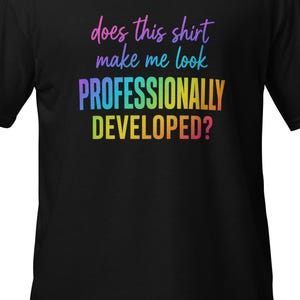 Può includere: Una t-shirt nera a maniche corte con il testo multicolore "does this shirt make me look PROFESSIONALLY DEVELOPED?" stampato sul davanti. Le lettere utilizzano una sfumatura di tonalità rosa, blu, giallo e arancione sul tessuto scuro.