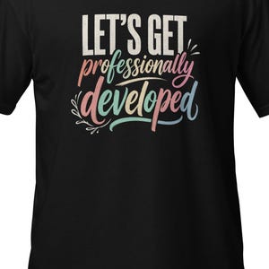May include: A black short-sleeved t-shirt featuring the text "LET'S GET professionally developed" printed on the chest. The word "LET'S GET" is in white, while "professionally developed" is written in a multi-colored script font with floral accents.