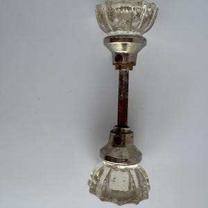 May include: A vintage door knob with clear, faceted glass knobs and a tarnished metal base. The connecting rod is rusty. The knobs have a flower-like design. The door knob is against a white background.