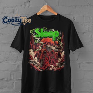 May include: A black short-sleeved t-shirt featuring a graphic print of hooded figures in red robes walking through a desert landscape with a large orange planet, green smoke, and the word Sleep in green letters above the scene.