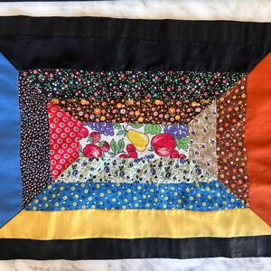 Puede incluir: Una colcha de retazos colorida con un borde negro. La colcha está hecha de varias telas con patrones florales y geométricos. La colcha tiene una forma rectangular y una combinación de colores amarillo, azul y rojo.