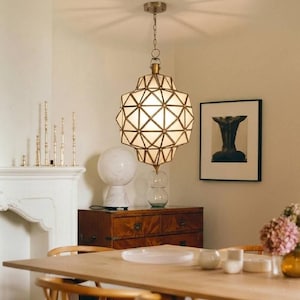 May include: A geometric pendant light fixture with a brass finish hangs from the ceiling. The light has a multi-faceted design with white panels. The room also features a wooden dresser, a marble lamp, and a framed artwork.