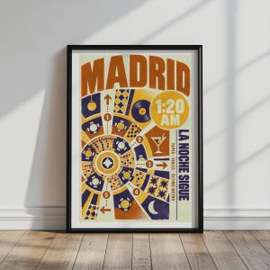 May include: A framed poster titled MADRID featuring a circular graphic design with orange, yellow, and dark blue geometric patterns. It includes the text 1:20 AM, LA NOCHE SIGUE, TAPAS, VINILO, and ÚLTIMO METRO, alongside icons of a martini glass and vinyl record.