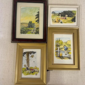 May include: A collection of framed illustrations featuring scenes with a boy and a yellow bear. The artwork is in various gold and dark red frames. The illustrations depict outdoor scenes with a warm color palette.