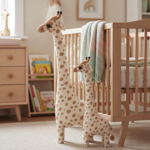 Pode incluir: Dois bichos de pelúcia de girafa, um grande e outro pequeno, lado a lado. As girafas têm manchas marrons em um fundo creme. Estão em um quarto de bebê com um berço e uma cômoda de madeira.