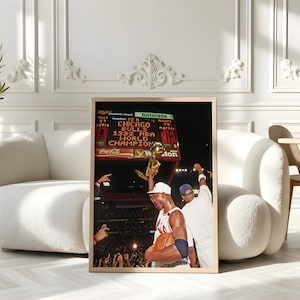 May include: A framed vertical photograph depicting a basketball player in a white jersey holding a gold trophy aloft. The scoreboard in the background displays the text Chicago Bulls 1992 NBA World Champions. The scene captures a stadium celebration.
