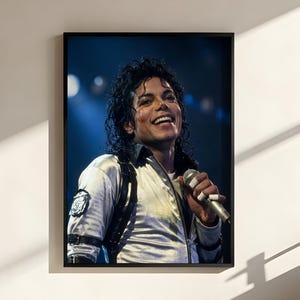 May include: Framed portrait of a smiling man holding a microphone, wearing a white jacket with black accents. The background is a stage with blue lighting. The image is in a black frame.