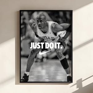 Peut inclure: Une affiche murale encadrée en noir et blanc représentant un joueur de basket-ball en maillot, accroupi en position défensive. Le texte JUST DO IT. est imprimé en lettres capitales blanches au-dessus du logo Nike blanc centré.