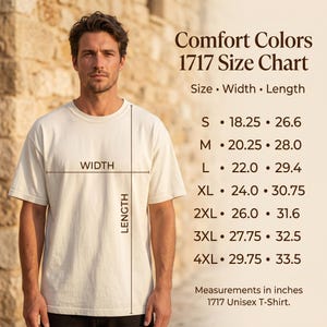May include: A person wearing a cream-coloured Comfort Colors 1717 Unisex T-Shirt. The image includes a size chart with measurements in inches for sizes S through 4XL. The chart shows width and length measurements for each size.