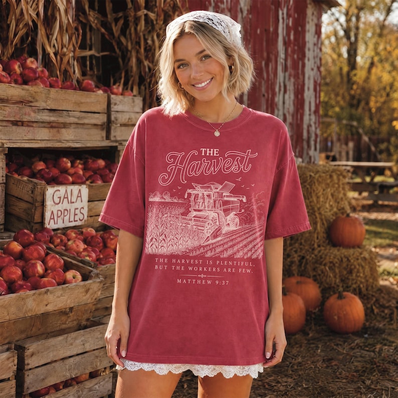 May include: A red short-sleeved t-shirt featuring a white graphic of a combine harvester in a field with the text The Harvest, The harvest is plentiful, but the workers are few, and Matthew 9:37. The shirt has a white lace trim at the bottom hem.