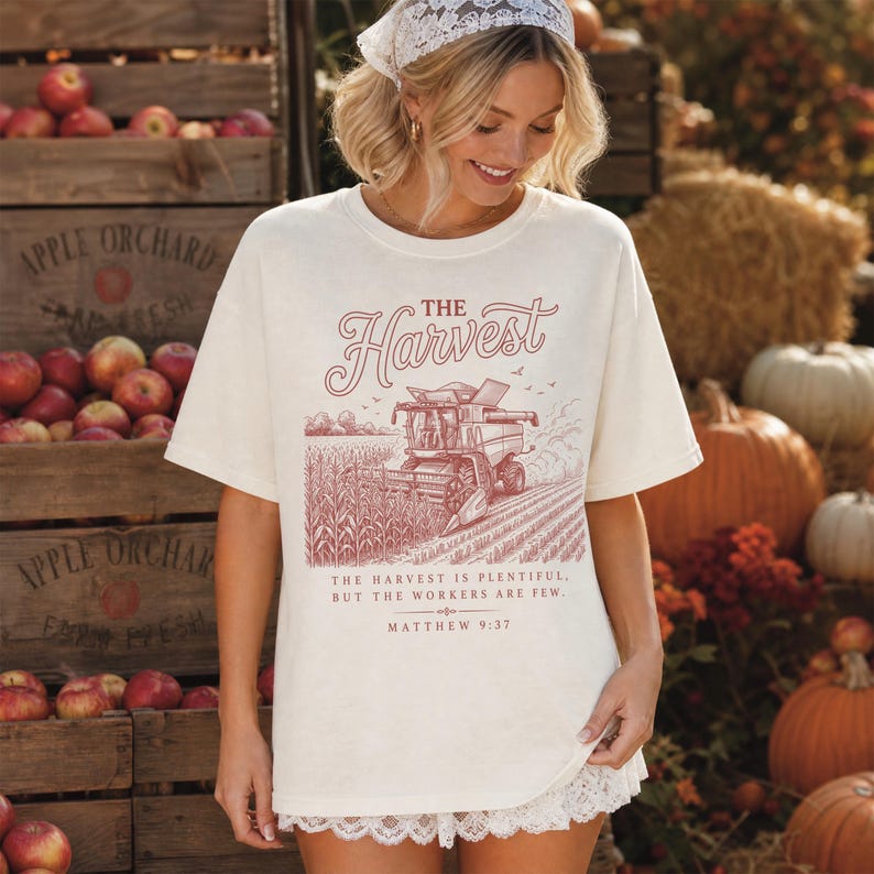 May include: An off-white short-sleeve t-shirt featuring a red graphic of a combine harvester in a cornfield. The text reads THE HARVEST, THE HARVEST IS PLENTIFUL, BUT THE WORKERS ARE FEW, and MATTHEW 9:37. The shirt has a crew neckline and a relaxed fit.