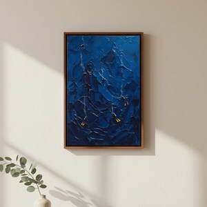 May include: Abstract blue oil painting in a wooden frame. The artwork features textured brushstrokes in varying shades of blue, creating a sense of depth and movement. The painting is displayed on a white wall above a wooden cabinet.