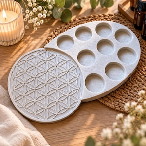 Könnte beinhalten: Ein hellgraues, gesprenkeltes, ovales Tablett mit einem kreisförmigen Bereich, der ein geprägtes geometrisches Lebensblumenmuster aufweist, sowie einem weiteren Bereich mit neun kreisförmigen Vertiefungen für kleine Gegenstände.