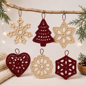 Pode incluir: Seis ornamentos de crochê pendurados em um galho, incluindo um floco de neve bege, uma árvore de Natal vermelho-escura, uma estrela bege, um coração vermelho-escuro, um medalhão circular bege e um floco de neve hexagonal vermelho-escuro.