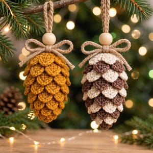 May include: Two hanging ornaments shaped like pinecones, crafted from crocheted yarn. One is solid mustard yellow, the other features alternating rows of cream and dark brown. Each has a natural wooden bead and a jute twine bow at the top.