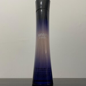 Peut inclure: Un flacon de parfum long et fin avec un dégradé de couleurs, passant du bleu foncé à la base au rose clair en haut. Le flacon a un bouchon noir et les mots "Armani Code" sont imprimés sur le devant.