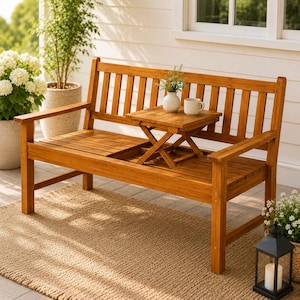 May include: A light brown wooden bench featuring a slatted backrest, armrests, and a built-in square folding table positioned in the center of the seat. The table holds a small white ceramic vase with greenery and a white mug.