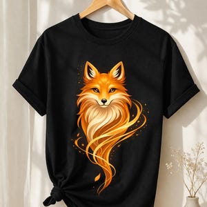 Könnte beinhalten: Schwarzes T-Shirt mit einer Illustration eines orangefarbenen Fuchses. Der Fuchs hat detailliertes Fell und ist von fließenden orangefarbenen Linien umgeben. Das T-Shirt ist an der Taille geknotet und hängt an einem Holzkleiderbügel.