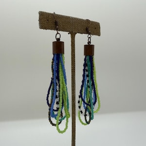 May include: A pair of dangle earrings featuring multiple strands of small seed beads in shades of lime green, turquoise, navy blue, and white. Each earring is attached to a copper-toned metal cap and a hook wire for hanging from the ear.