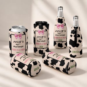 May include: A collection of beverage insulators featuring a black and white cow print pattern. Some insulators display a pink bow and text reading JULIE'S 40TH BIRTHDAY CHEERS TO 40 YEARS 2026, while others are personalized with the name AMELIA.