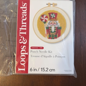 May include: A Loops & Threads punch needle kit in a clear plastic bag. The packaging features a 6 inch nutcracker design in a wooden embroidery hoop, with red, green, and yellow yarn colors. The text reads Loops & Threads, Christmas, Noel, Punch Needle Kit, and 6 in / 15.2 cm.