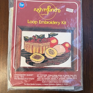 May include: A Boye Rush 'N Punch Loop Embroidery Kit in a clear plastic bag. The packaging features a red background with the text 'Strawberry Basket' and 'Fits Standard 5"x7" Frame'. The design shows a basket of strawberries and fruit.