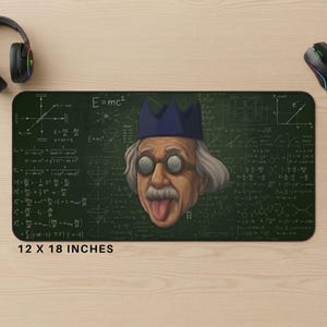 May include: A rectangular desk mat measuring 12 by 18 inches featuring a dark green background covered in white physics equations and diagrams. Centered is a cartoon illustration of a scientist with gray hair, goggles, and a blue crown.